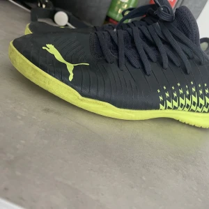 Svarta och gula futsal/ inneskor från Puma - Säljer ett par coola futsal från Puma i svart och gult. Skorna har snörning och en snygg design med mönster på sidan. Perfekta för fotbollsträningen eller matchen. Använda men i bra skick!