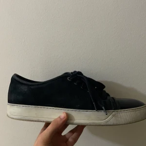 Lanvin skor - Säljer ett par svarta sneakers i mocka med vit sula. De har snörning och en stilren design som passar perfekt till vardags. Skorna är i välanvänt skick men fortfarande snygga och bekväma. Perfekta för både vår och höst!