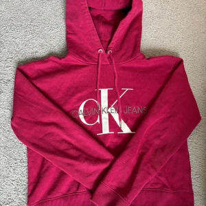 Röd hoodie från Calvin Klein Jeans - Säljer en snygg vinröd hoodie från Calvin Klein Jeans i storlek S. Den har en klassisk design med CK-logga på framsidan och justerbar huva med dragsko. Perfekt för en avslappnad stil eller kyliga dagar. 🫶🏻