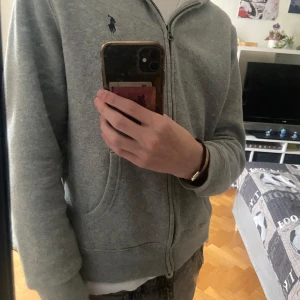 Raulph Lauren grå zip hoodie - Säljer denna Raulph Lauren tröja i storlek 14-16. Fick den i present och den passade tyvärr inte. Jag på bilden är ca 175 och ganska smal, tröjan passar strl 170. Skick 10/10 då den är helt oanvänd. Tveka inte att skriva vid frågo eller funderingar! 