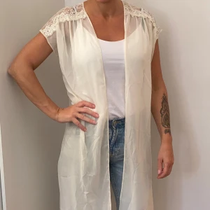 Vit spetsdetaljerad kimono från Monki - Säljer en superfin vit kimono från Monki i storlek medium. Den har vackra spetsdetaljer vid axlarna och är perfekt att ha över en topp eller klänning. Materialet är lätt och luftigt, vilket gör den idealisk för sommarens varma dagar. Perfekt för en avslappnad men stilren look!