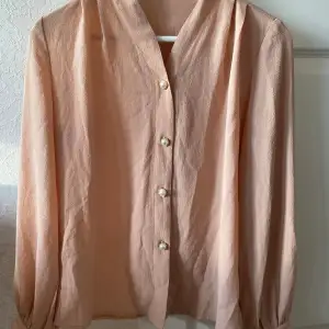 Säljer en superfin beige/rosa blus med långa ärmar och snygga pärlknappar framtill. Perfekt för både vardag och fest! Materialet känns lätt och luftigt, vilket gör den perfekt för vår och sommar.