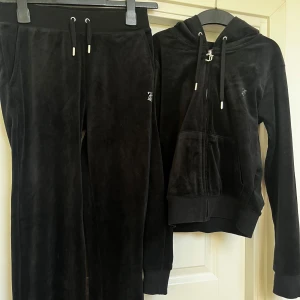 Mjukisdress  - Mjukisbyxor i XS : Elastisk dragsko i midjan  -Sidofickor  -Strassprydd logga  -Rak passform   Huvtröja storlek S : Huva med dragsko  -Stängning med dragkedja  -Strassprydd logga  -Sidofickor  -Regularfit/normal passform  