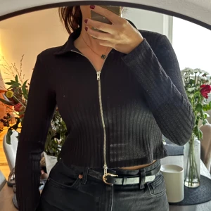 Svart kofta från Nelly - Säljer en snygg svart ribbad tröja från Nelly. Den är croppad och har en dragkedja framtill, storlek S 🤍