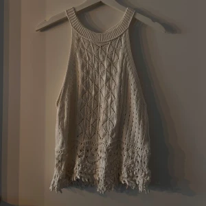 Vit stickad topp från Holly & Whyte - Säljer en superfin vit stickad topp från Holly & Whyte by Lindex. Den har ett snyggt mönster och är ärmlös med en liten knappdetalj i nacken. Toppen har en luftig och bekväm passform