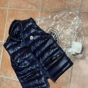 Moncler Gui väst  - Säljer nu min marinblåa Moncler Gui då jag vill ha en ny väst. Fint skick knappt änvänd Kan bytas mot jacka/väst Påse och lappar följer med Priset är ej fast:)