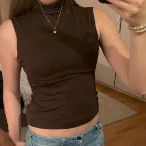 Brun ärmlös polotopp från Zara - Säljer en snygg brun ärmlös polotopp från Zara. Den är i storlek M och är tillverkad av 92% nylon och 8% spandex, vilket gör den både bekväm och stretchig. Perfekt för en stilren look!