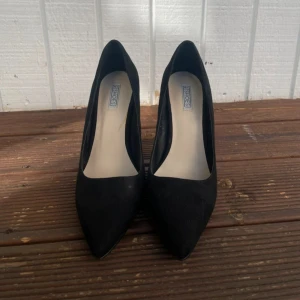 Klackskor  - Snygga svarta pumps i mocka från Nelly. De har en elegant spetsig tå och en smal klack som ger en stilren look. Perfekta för både fest och mer formella tillfällen. Skorna är i bra skick!