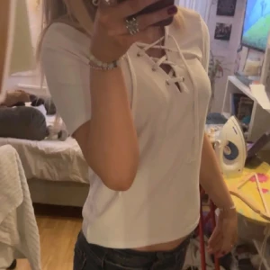 Vit topp med snörning - Säljer en snygg vit topp med korta ärmar och en cool snörning framtill. Perfekt för sommardagar eller en avslappnad utekväll. Toppen har en normal passform och är superbekväm att bära.