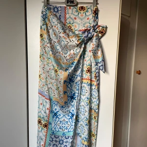 Häftig långkjol  - Väldigt vacker kjol som jag helst inte vill sälja men tyvärr är den för liten. Glansigt material, fint mönster och en snörning på sidan. Den har även en dragkedja.