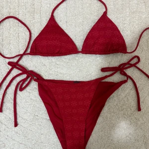 Röd bikini med blommbrodyr(ej använd) - Snygg röd bikini (S) med blommönster och knytband. Perfekt för sommaren! Toppen har trekantsform och underdelen har knyt i sidorna för justerbar passform. 🌺Den är inte använd endast testad men var för liten för mig. Den är från NAKD! Ord pris= 450kr säljs för= 200