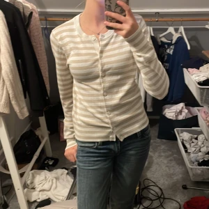 Beige och vit randig kofta från H&M - Säljer en superfin beige och vit randig kofta från H&M i storlek XS. Den är i mycket bra skick och har långa ärmar med knappar hela vägen fram. Perfekt för både vår och höst! 🧥✨