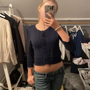 Mörkblå bolero - Säljer en superfin mörkblå stickad kofta med knappar framtill. Den är croppad och har ett snyggt flätmönster. Perfekt för höst och vår när du vill ha något mysigt men ändå stilrent. Passar bra till både jeans och kjol!