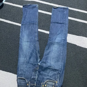 Blå jeans från Levi's - Säljer ett par klassiska blå jeans från Levi's i bra skick. De har en straight passform och är tillverkade i slitstarkt denim. Perfekta för vardagsbruk och kan enkelt matchas med olika outfits. Jeansens ikoniska röda etikett syns tydligt på bakfickan.