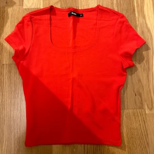 Röd kortärmad topp från Bik Bok - Snygg röd topp från Bik Bok i storlek XS. Den har en enkel och stilren design med korta ärmar och en rundad halsringning. Perfekt för både vardag och fest!