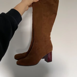Bruna mockastövlar  - Säljer ett par bruna stövlar i mocka med transparent klack i rödbrun nyans. Köpta på Sellpy. I bra skick, enda defekt är ”skrap” på klacken (se bild 4).