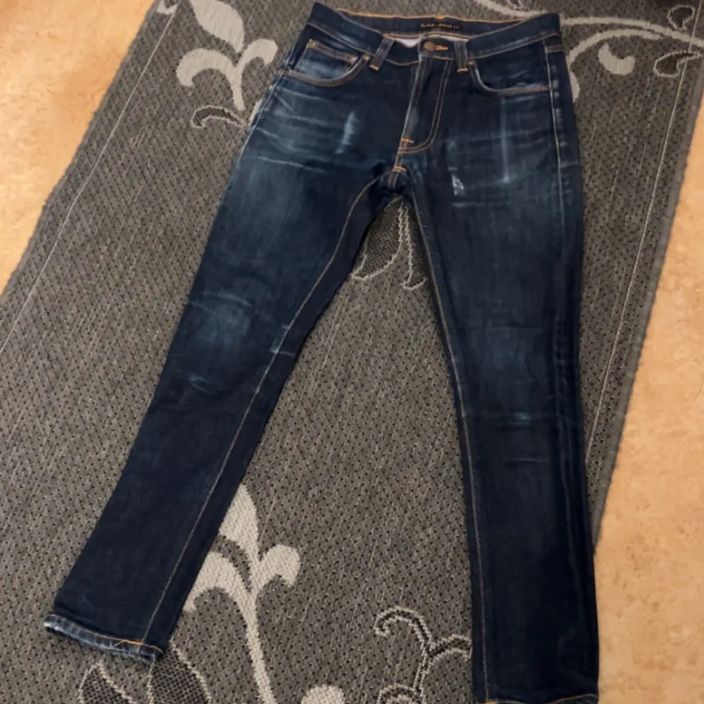 Säljer ett par snygga mörkblå jeans från Nudie Jeans i storlek 27/30. De har en slim passform och klassisk femficksdesign med orange sömmar och broderade bakfickor. Perfekta för både vardag och fest! 🕺 . Jeans & Byxor.