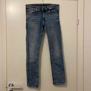 Blå jeans från Tommy Hilfiger - Säljer ett par snygga blå jeans från Tommy Hilfiger i storlek 164. De har en klassisk slim fit och är i mycket bra skick. Perfekta för både vardag och fest! Jeansmaterialet är slitstarkt och bekvämt, med en stilren design och ikoniska Tommy Hilfiger-detaljer.