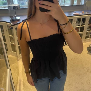 Svart axelbandslös topp - Säljer en superfin mörkblå topp med knytbara axelband. Den har en smockad överdel som ger en tight passform upptill och en luftigare nederdel med volang. Storlek S🥰