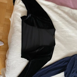 Svart sammetstopp - Säljer en elegant svart sammetstopp med långärmad design. Perfekt för en kväll ute eller en fest. Toppen har en mjuk och lyxig känsla tack vare sammetstyget. Passar bra till både jeans och kjol för en stilren look.