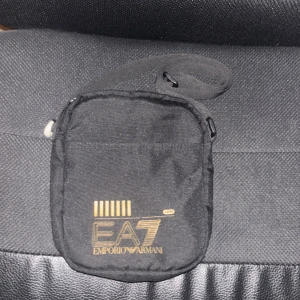 Svart axelväska från Emporio Armani - Säljer en stilren svart axelväska från Emporio Armani. Väskan har en praktisk dragkedja och justerbar axelrem. Perfekt för både vardag och fest! 🖤