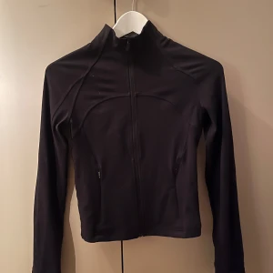 Svart jacka från Lululemon - Säljer en svart, super snygg jacka från Lululemon i mycket bra skick. Den har en dragkedja framtill och långa ärmar. Perfekt för träning eller som en lätt jacka under vår och höst💞💞Är även öppen för byten mot andra lululemon!!