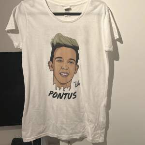 Säljer en vit t-shirt med ett stort tryck av en tecknad person och texten 'Pontus' på framsidan. Baksidan har texten 'Pontus Rasmusson'. T-shirten är kortärmad och i bomull, perfekt för vardagsbruk. Den är även signerad av Pontus är 2019!!!!