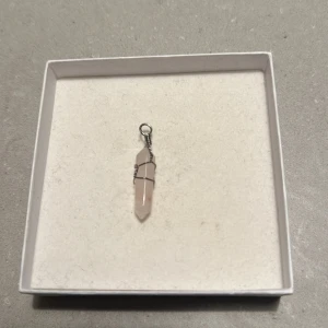 Rosa kristallhalsband - Säljer ett vackert rosa kristallhalsband med en spetsig form. Kristallen är omsluten av en tunn metalltråd som ger en stilren look. Perfekt för att ge en touch av elegans till din outfit. 