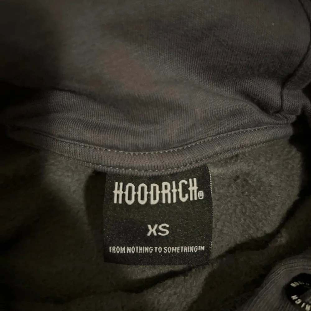 Säljer en grå hoodie från Hoodrich i mycket bra skick. Den har en cool design med svart text på framsidan och en världskarta i guld på baksidan. Hoodien har en stor ficka fram och vita detaljer på ärmarna. Perfekt för höst och vinter!. Tröjor & Koftor.