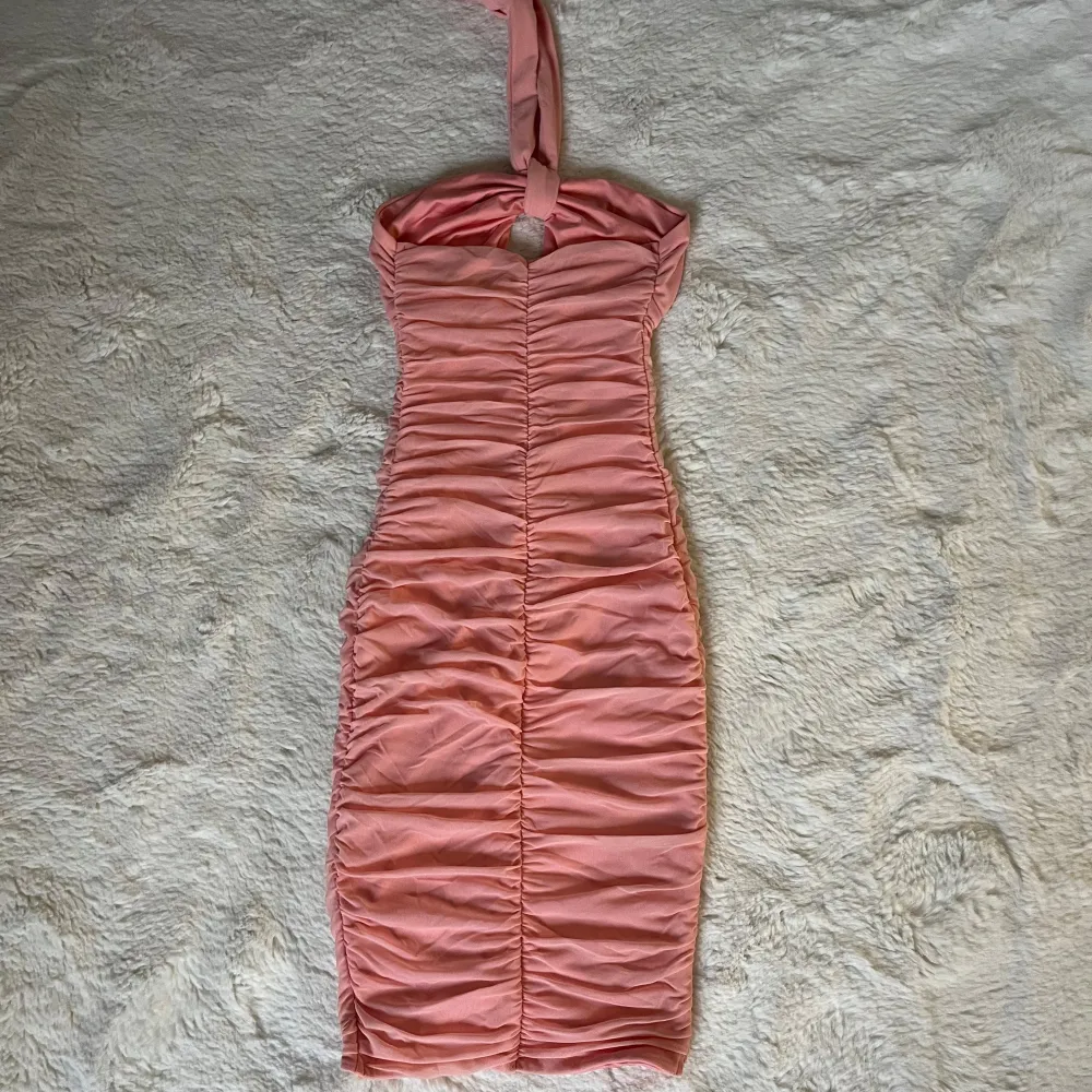 Säljer en superfin rosa axelbandslös klänning med halterneck-knytning. Den har en tight passform och är rynkad längs hela klänningen för en smickrande look. Perfekt för sommarens fester eller en utekväll. Klänningen är i mycket bra skick och redo att bäras av någon som vill sticka ut!. Klänningar.