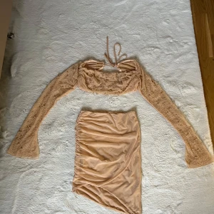 Beige tvådelad klänning med pärlor - Säljer en superfin tvådelad klänning i beige från Oh Polly. Toppen har långa ärmar och är dekorerad med pärlor och snörning i ryggen. Kjolen är kort och har en snygg rynkad design. Perfekt för fest eller speciella tillfällen! ✨