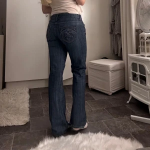 Blå jeans med broderad bakficka - Midjemått rakt över = 39cm  Innerbenslängd = 78cm Från grenen till midjan = 15cm           Säljer ett par snygga blå jeans med coolt broderi på bakfickorna. De är lågmidjade och har en bootcut-stil. 