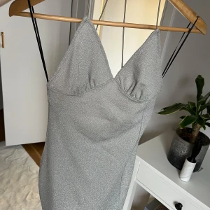 Glittrig silverklänning - Snygg glittrig silverklänning med smala axelband och en figurnära passform. Perfekt för festliga tillfällen! Klänningen har en elegant design med en lätt skimrande yta som fångar ljuset fint.