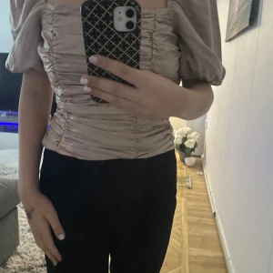 Beige offshoulder topp - Säljer en superfin beige offshoulder topp med puffiga ärmar. Den har en åtsittande passform med rynkade detaljer som ger en snygg siluett. Perfekt för en utekväll eller fest! 🥳