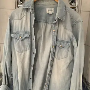 Säljer en snygg ljusblå jeansskjorta från Pull & Bear i storlek M. Skjortan har långa ärmar och knappar framtill samt på bröstfickorna. Perfekt för en avslappnad stil och kan bäras som en overshirt. 