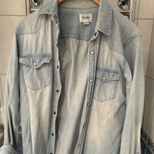 Ljusblå jeansskjorta från Pull & Bear - Säljer en snygg ljusblå jeansskjorta från Pull & Bear i storlek M. Skjortan har långa ärmar och knappar framtill samt på bröstfickorna. Perfekt för en avslappnad stil och kan bäras som en overshirt. 