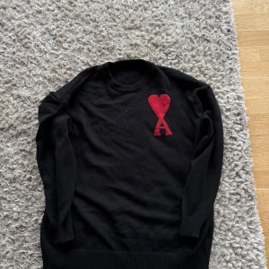 Svart tröja med rött hjärta - Säljer en svart tröja med ett rött hjärta och bokstaven 'A' på bröstet. Tröjan är långärmad och har en rund halsringning. Perfekt för både vardag och fest!