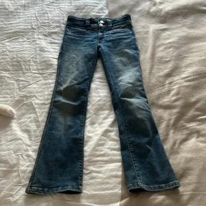 Blå bootcut jeans från H&M - Säljer ett par snygga blå bootcut jeans från H&M i storlek 146. De har låg midja och justerbar midja för perfekt passform. Det är backfickor med lock och knapp. Använda men i bra skick!