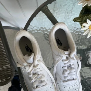 Vita Nike sneakers - Säljer ett par vita Nike sneakers i bra skick. De har en klassisk design med snörning och perforerade detaljer på ovansidan för ventilation. Perfekta för vardagsbruk och ger en stilren look. Lite slitna på sulan men fortfarande i gott skick.