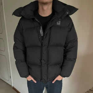 Svart pufferjacka från 66° North - Säljer min svarta pufferjacka från 66° North i storlek M. Den har en praktisk dragkedja och en hög krage för extra värme. 6900kr ny pris 