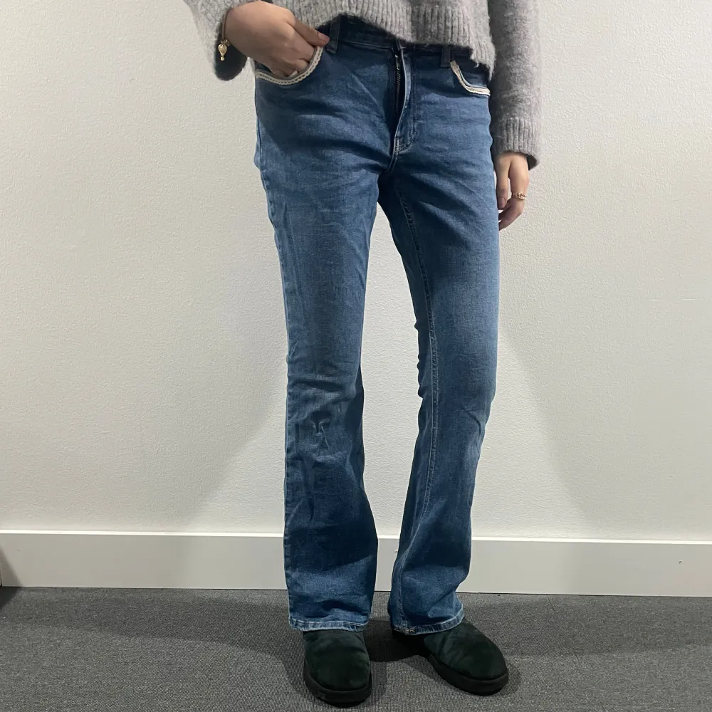 Säljer ett par snygga blå jeans från Gina Tricot. De har unika spetsdetaljer på fickorna både fram och bak, vilket ger dem en söt touch. De är lowaist och bootcut. Storlek: 38. Modellen är 178 cm lång.. Jeans & Byxor.