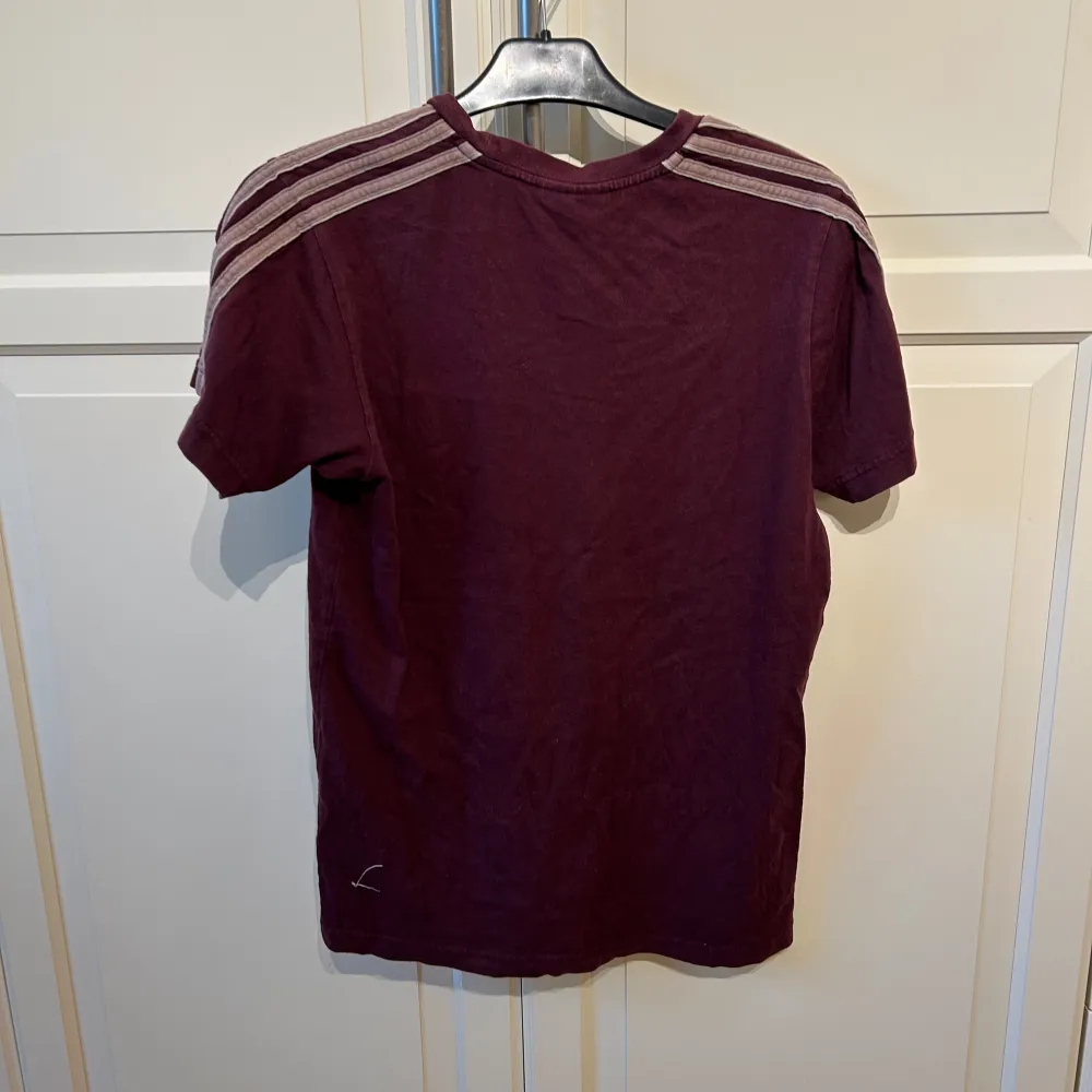 Säljer en snygg vinröd stora t-shirt från Adidas i mycket bra skick. Den har korta ärmar och klassiska Adidas-ränder på axlarna. Perfekt för både vardag och träning. Märket syns på bröstet och materialet är mjukt och bekvämt.. T-paidat.