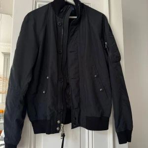 Svart bomberjacka från Polo Ralph Lauren - Säljer en snygg svart bomberjacka från Polo Ralph Lauren i storlek S. Jackan har en dragkedja och knappar framtill, samt ribbstickade muddar vid ärmslut och nederkant. Perfekt för höst och vår! Finns spår av användning men jackan är hel och mycket snygg! 