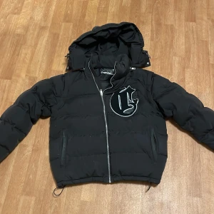 Svart pufferjacka med avtagbara ärmar - Säljer en svart pufferjacka från Corvidae med avtagbara ärmar och huva. Perfekt för både höst och vinter! Jackan har en dragkedja framtill och en cool logga på bröstet. Den är i bra skick och superpraktisk för olika väder. Passar perfekt för en casual look eller när du vill hålla dig varm och bekväm. Finns lite färgfläckar på jackan 