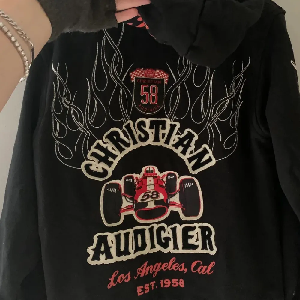 Säljer en svart hoodie från Christian Audigier med coola röda och vita tryck. Den har dragkedja fram och långa ärmar💗. Hoodies.