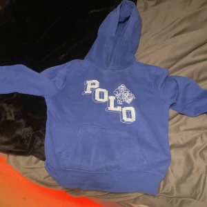 Blå hoodie från Ralph Lauren - Säljer en snygg blå hoodie från Ralph Lauren med stor POLO-logga och en cool bulldog på framsidan. Perfekt för en avslappnad stil och passar bra till både jeans och joggers. Den är i bra skick och superbekväm att ha på sig. Perfekt för höst och vår! Storlek är 10/12 cm 150 