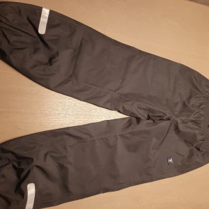 Svarta byxor från Polarn O. Pyret - Säljer ett par svarta byxor från Polarn O. Pyret i storlek 140. Byxorna har reflexdetaljer vid benen och är perfekta för utomhuslek. De är tillverkade i ett slitstarkt material och har en elastisk midja för bekväm passform.