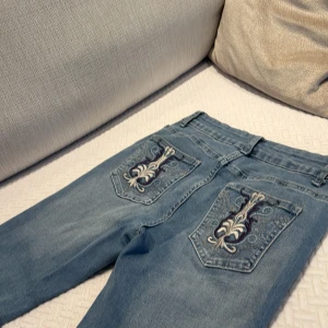 Blå jeans med broderade fickor - Säljer ett par snygga blå jeans med unika broderade detaljer på bakfickorna. De har en klassisk femficksdesign och en bekväm passform. Perfekta för både vardag och fest! 🦋