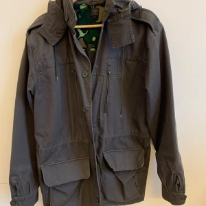 Fräsig jacka från Adidas - Säljer en svart jacka från Adidas i storlek L. Den har en cool camouflagemönstrad insida och är perfekt för höst och vår. Jackan har en huva och praktiska fickor framtill. Den är i mycket bra skick och redo för nya äventyr!