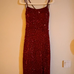 Röd glittrig långklänning - Säljer en fantastisk röd glittrig långklänning med smala axelband. Perfekt för nyårsfesten eller en glamorös kväll. Klänningen har en tight passform som framhäver figuren och ger en elegant look. Den är i mycket bra skick och redo att bäras av någon som vill glänsa!